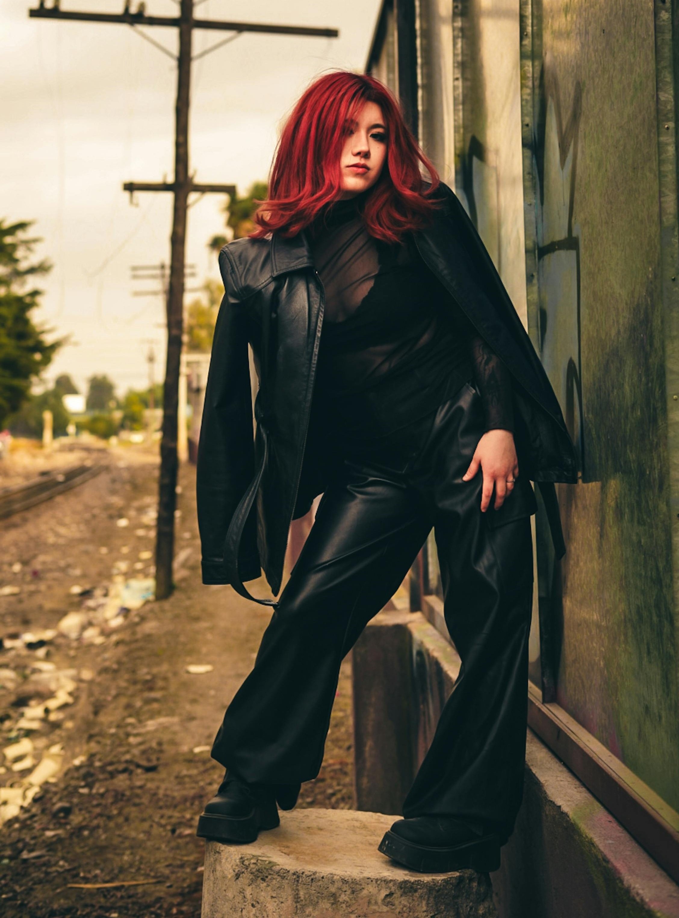 Person with red hair wearing a black leather jacket, sheer black top, black 
          leather-look pants, and chunky black shoes.