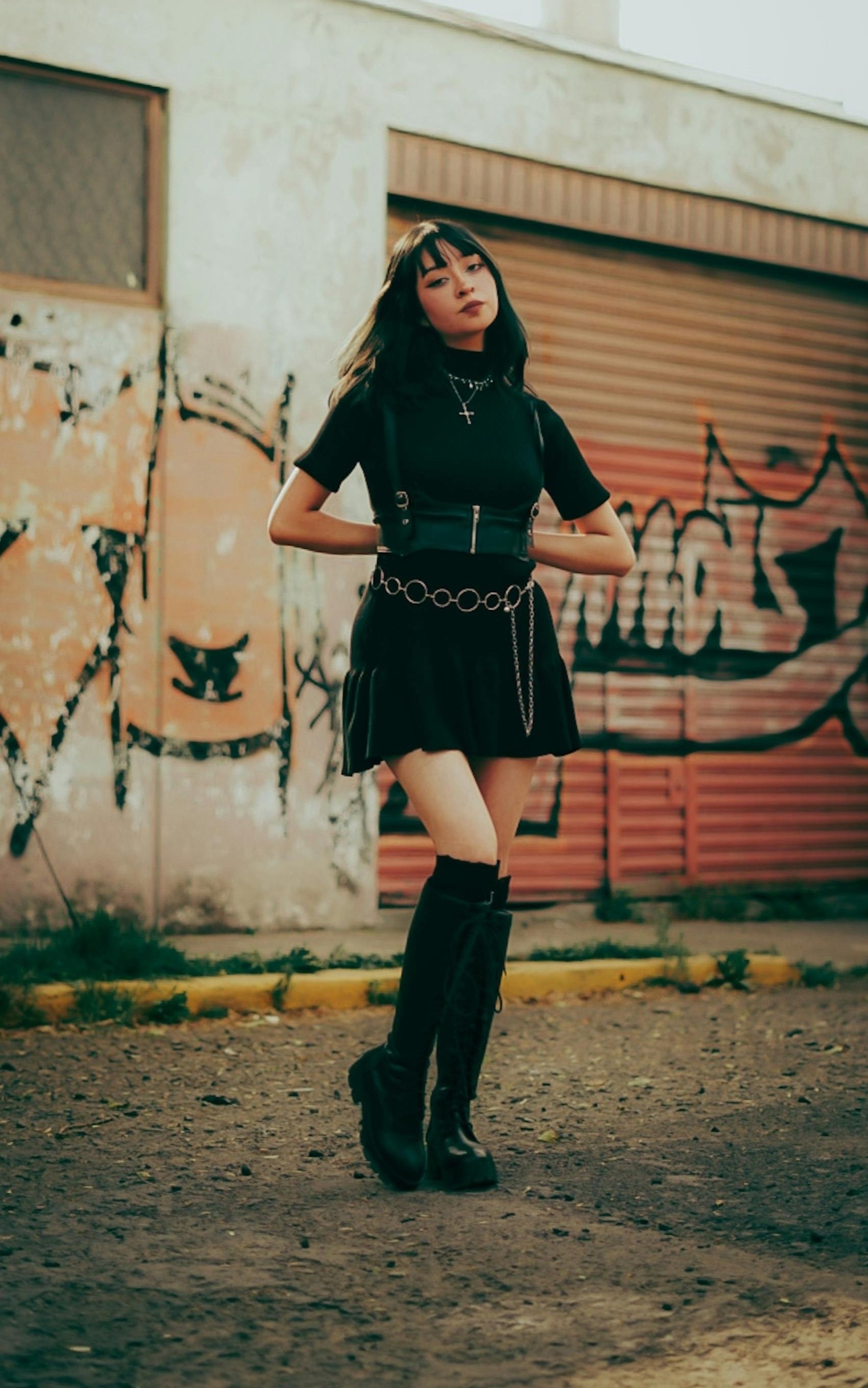 Black and white image of a person wearing a leather jacket, black crop top, 
          layered skirt, patterned tights, and platform boots.