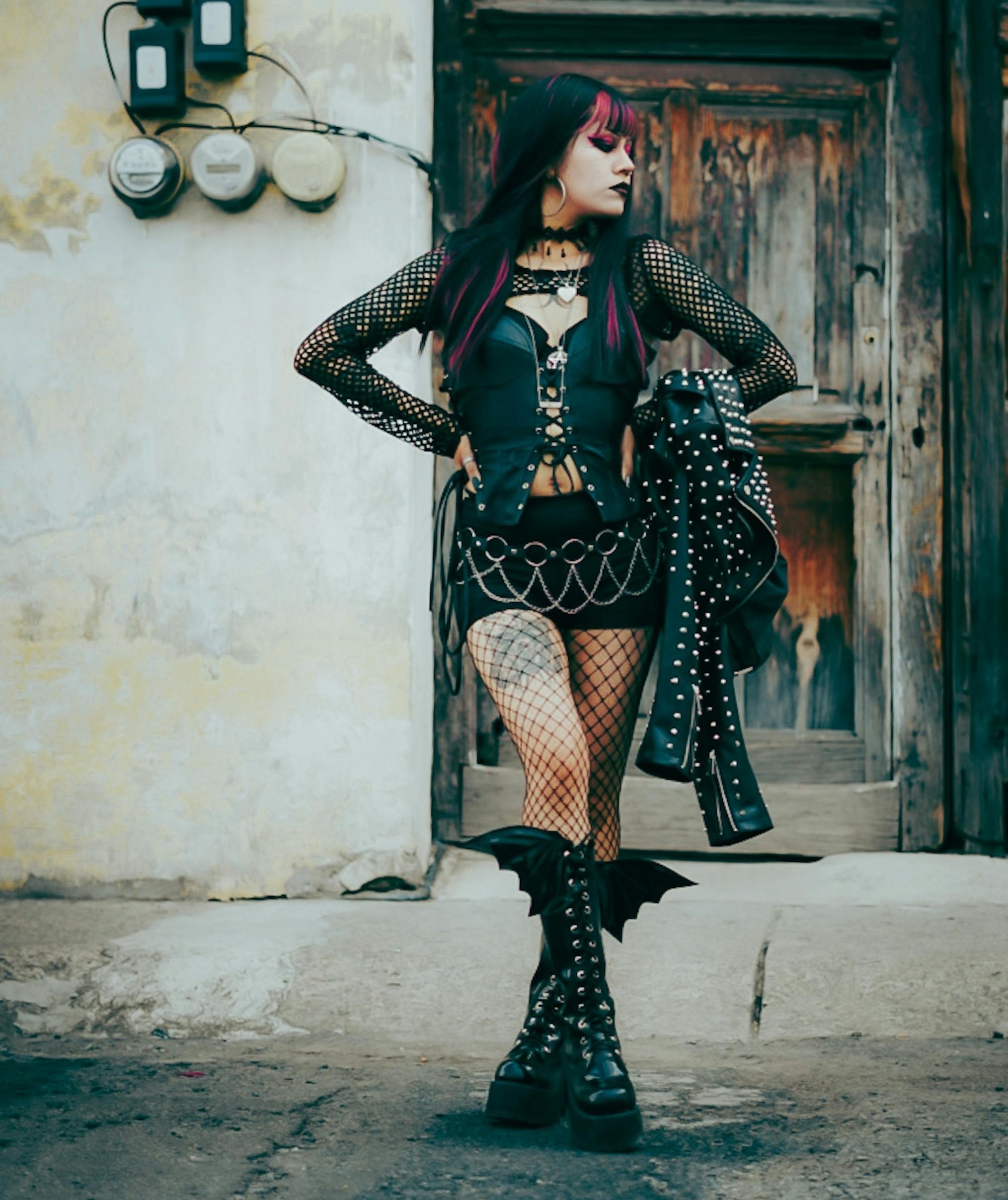 Person wearing a black lace-up top, black skirt, fishnet tights, chain belt, and tall black boots.