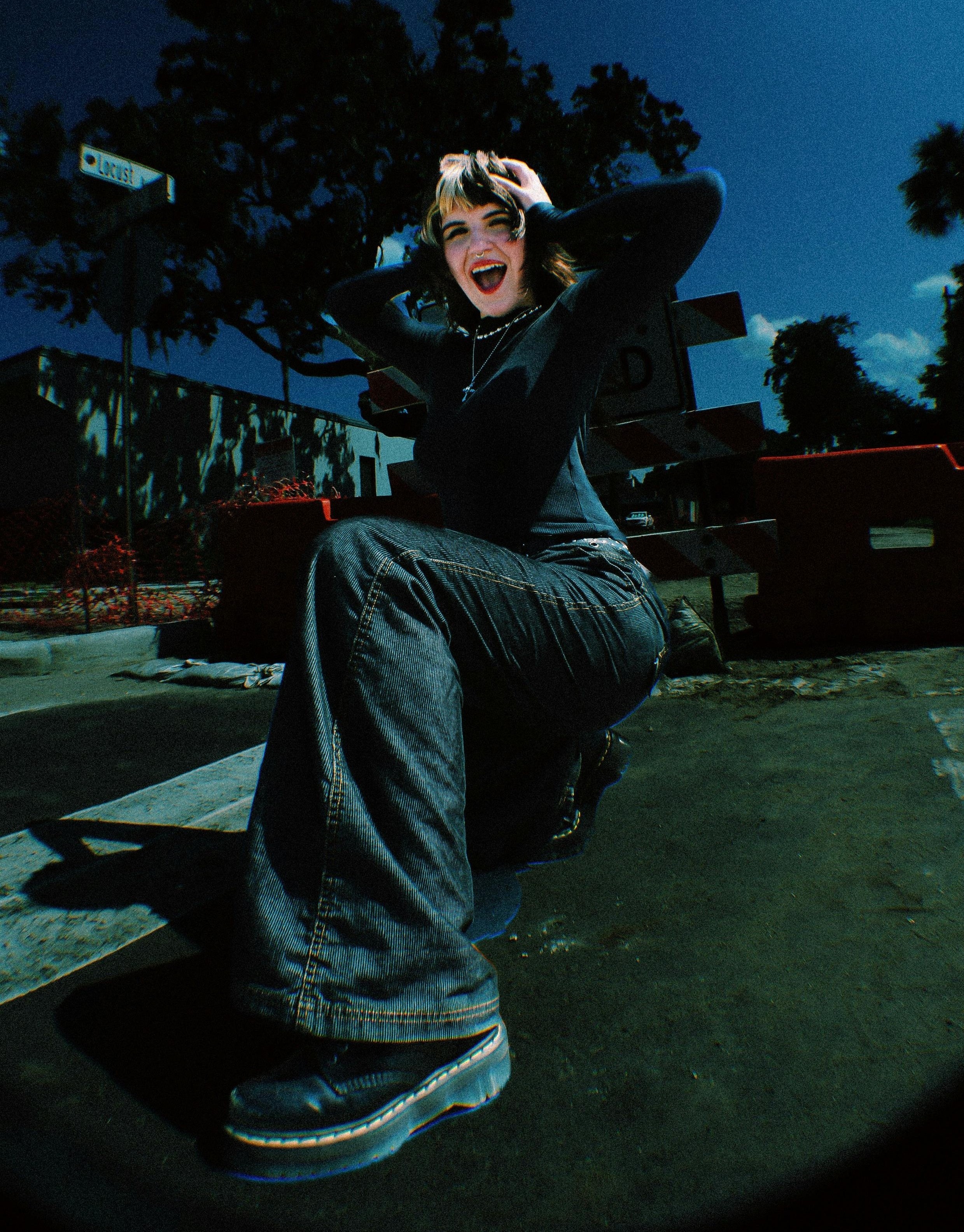Person crouching outside wearing a black long-sleeve top, wide-leg jeans, and black boots.