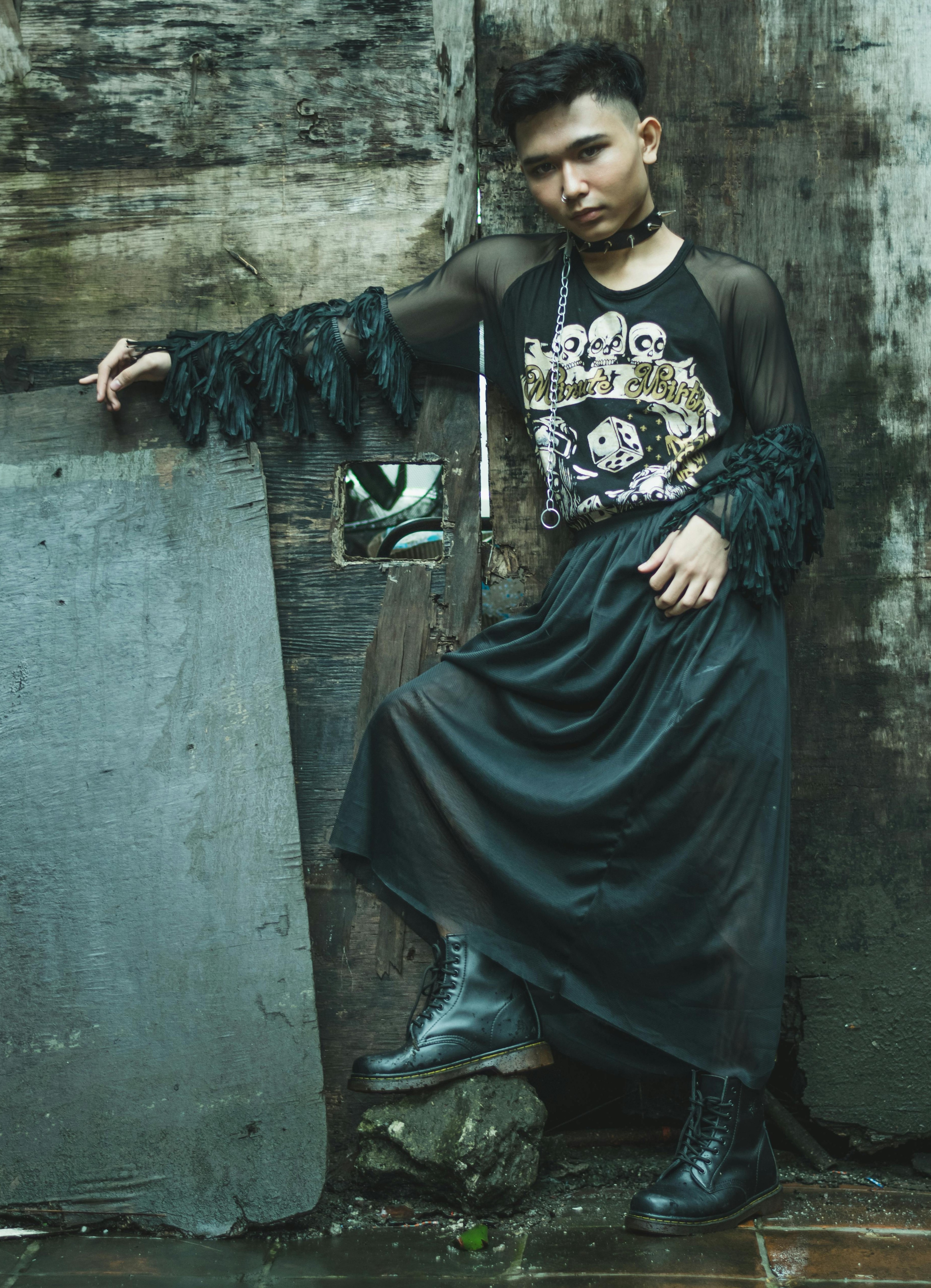 Person wearing a black graphic top with sheer sleeves, long black skirt, chain accessory, choker, and black boots.
