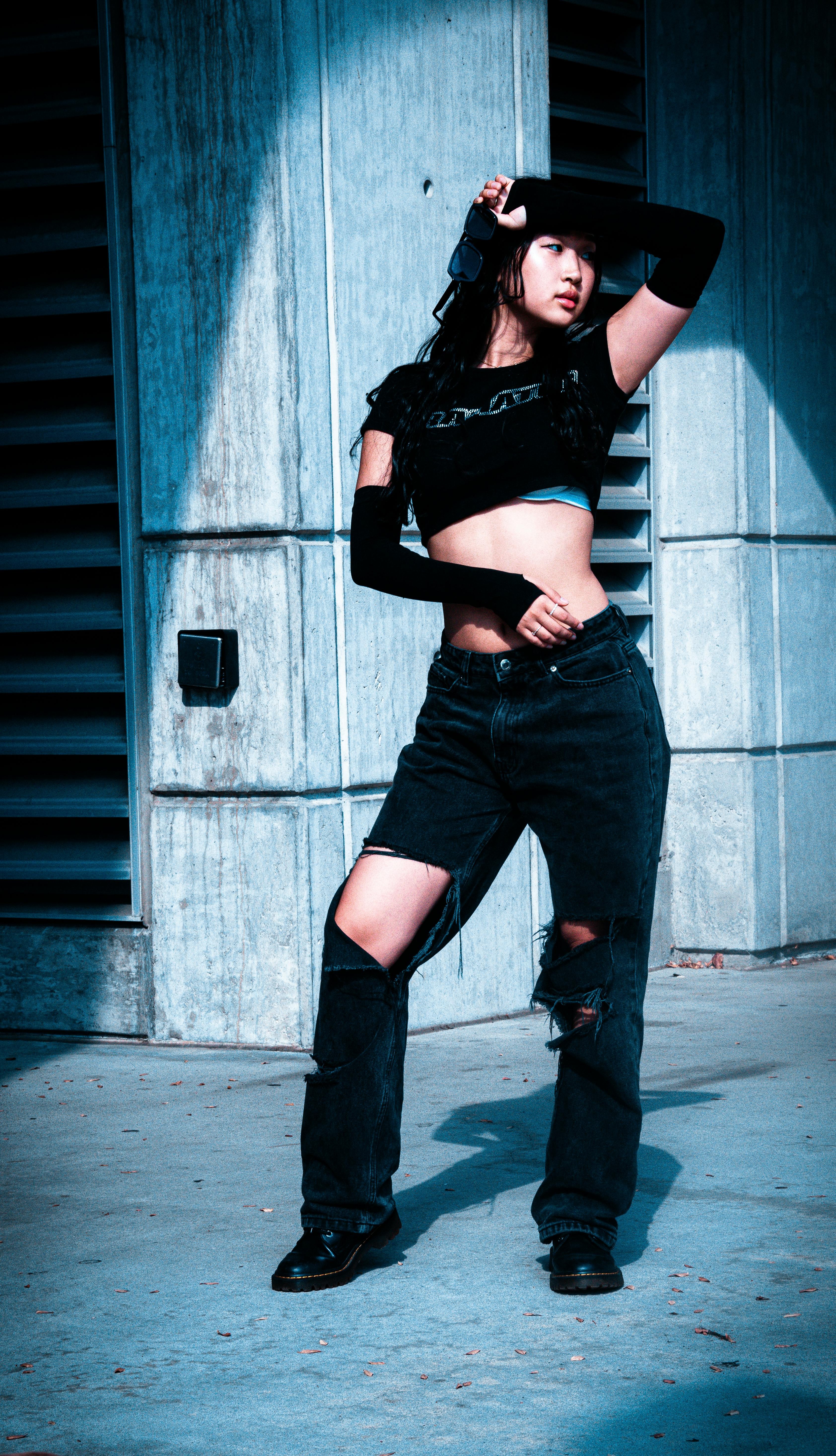 Person wearing a black crop top, ripped black jeans, long black arm warmers, and black boots.